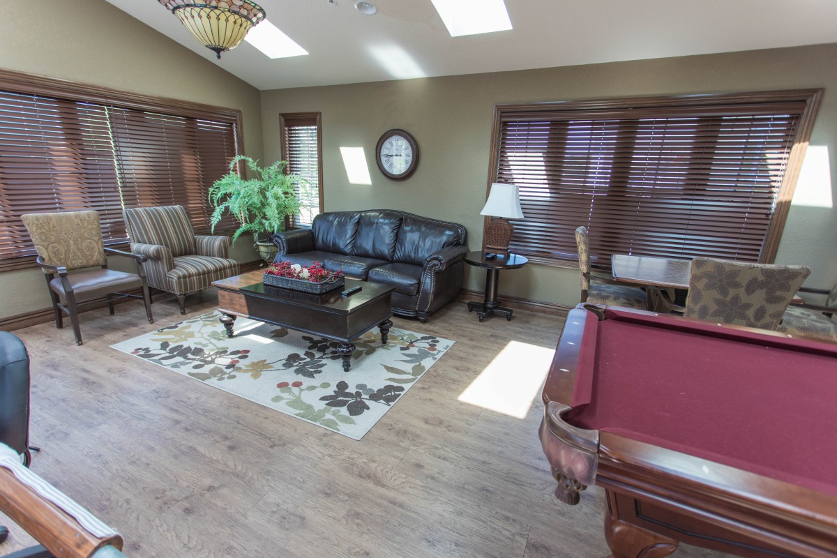 A cozy living room featuring a black leather sofa, armchairs, and a pool table.