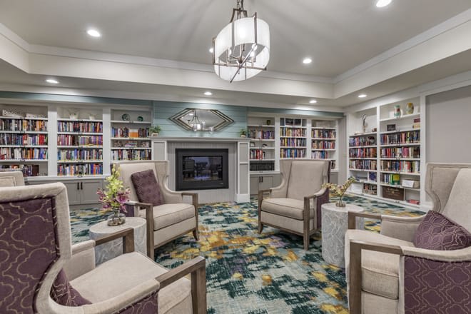 A cozy library room with comfortable armchairs, a fireplace, and bookshelves filled with books.