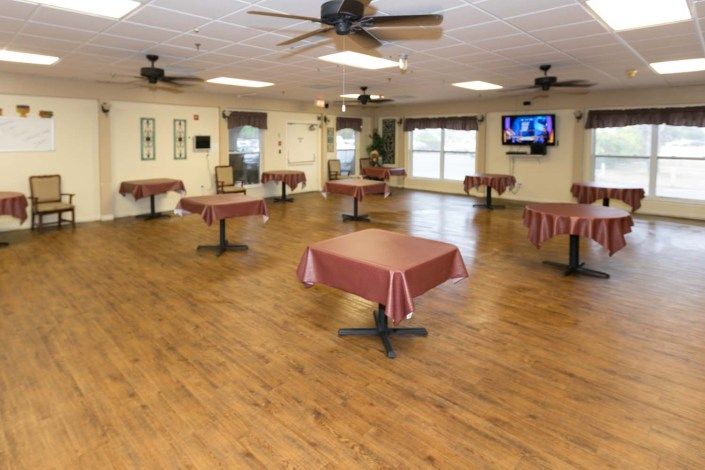 An empty dining room with tables and ceiling fans, featuring a wooden floor.
