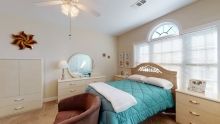 A cozy bedroom with a bed, dresser, and chair under natural light.