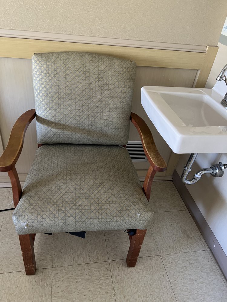 A chair positioned next to a small wall-mounted sink, likely in a hospital or waiting room setting.