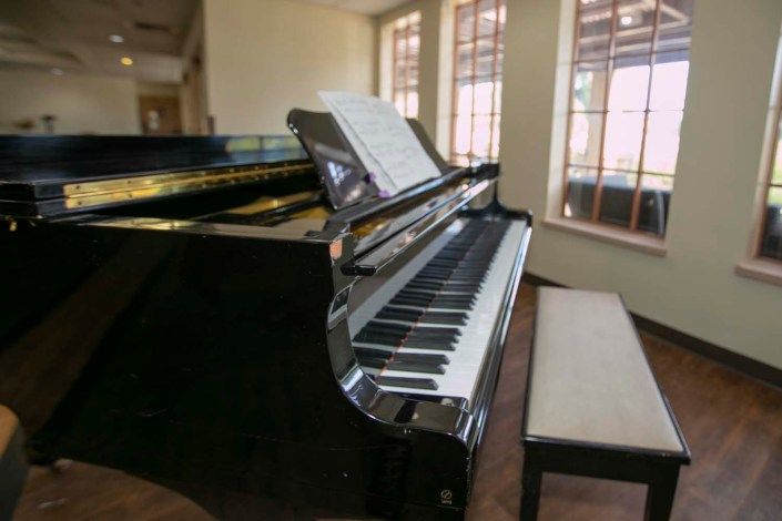 A piano with sheet music stands ready in a sunlit room.