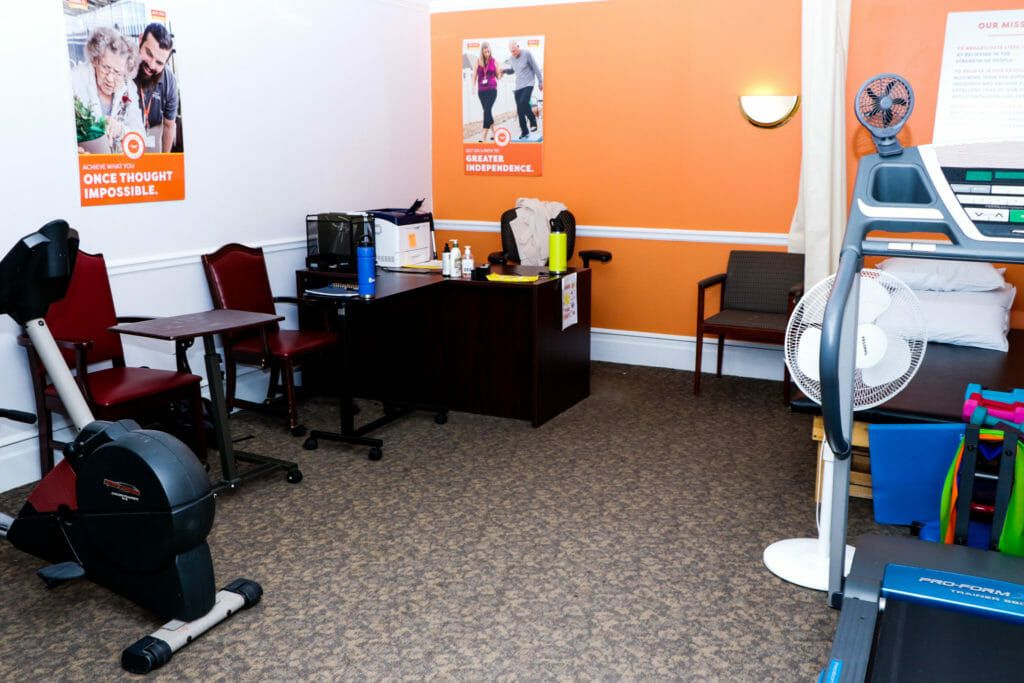 A small office space with a desk, chairs, and an orange accent wall featuring a poster.