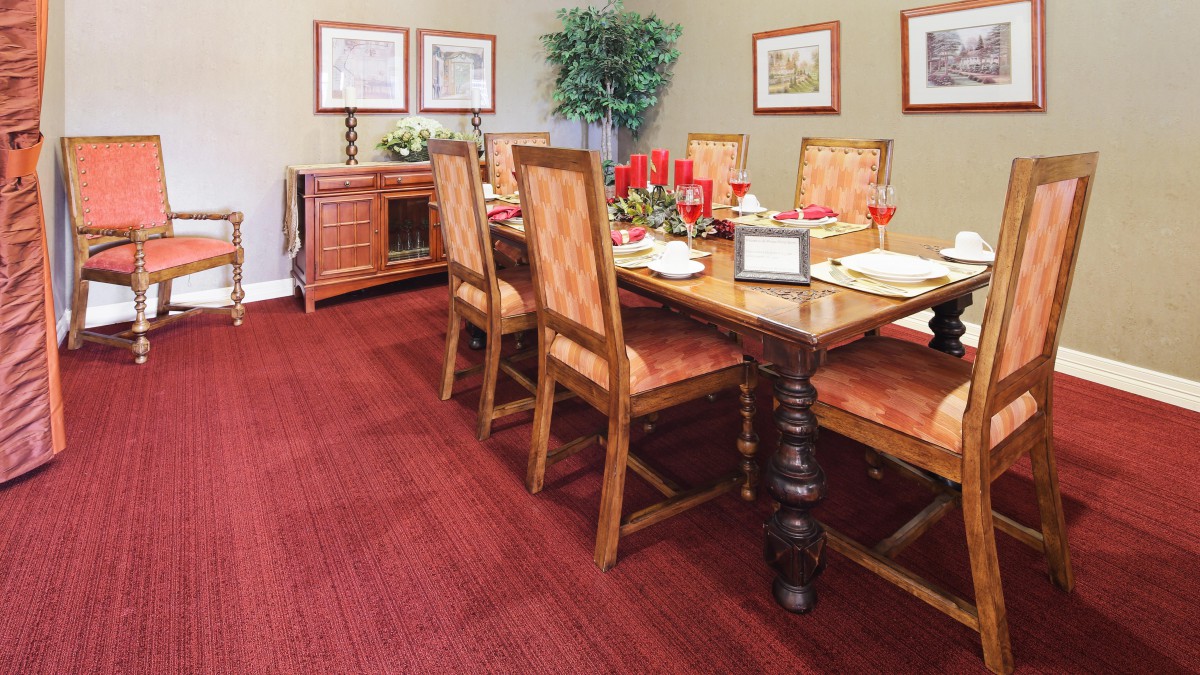 A well-decorated dining room with a wooden table, upholstered chairs, and a red carpet.