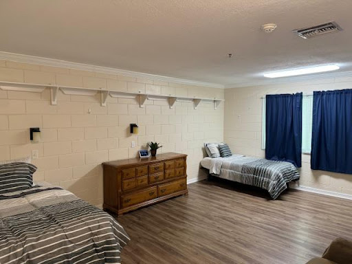 A spacious bedroom featuring two beds, a wooden dresser, and a blue curtain.