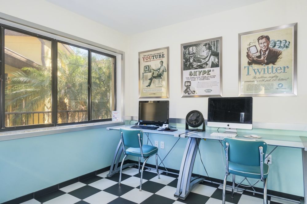 A retro-styled office space featuring vintage posters, a checkered floor, and computers on a sleek desk.