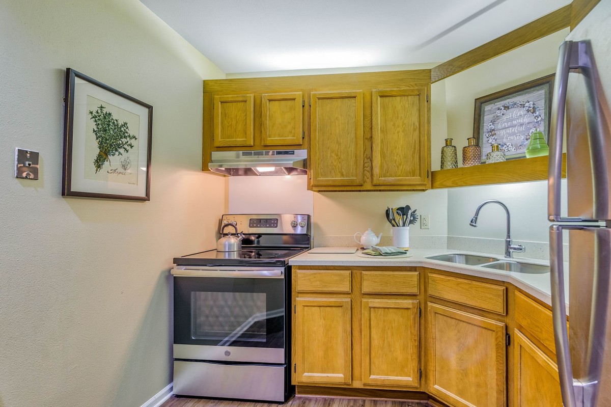 A compact kitchen with wooden cabinets, a modern stove, and a corner sink.