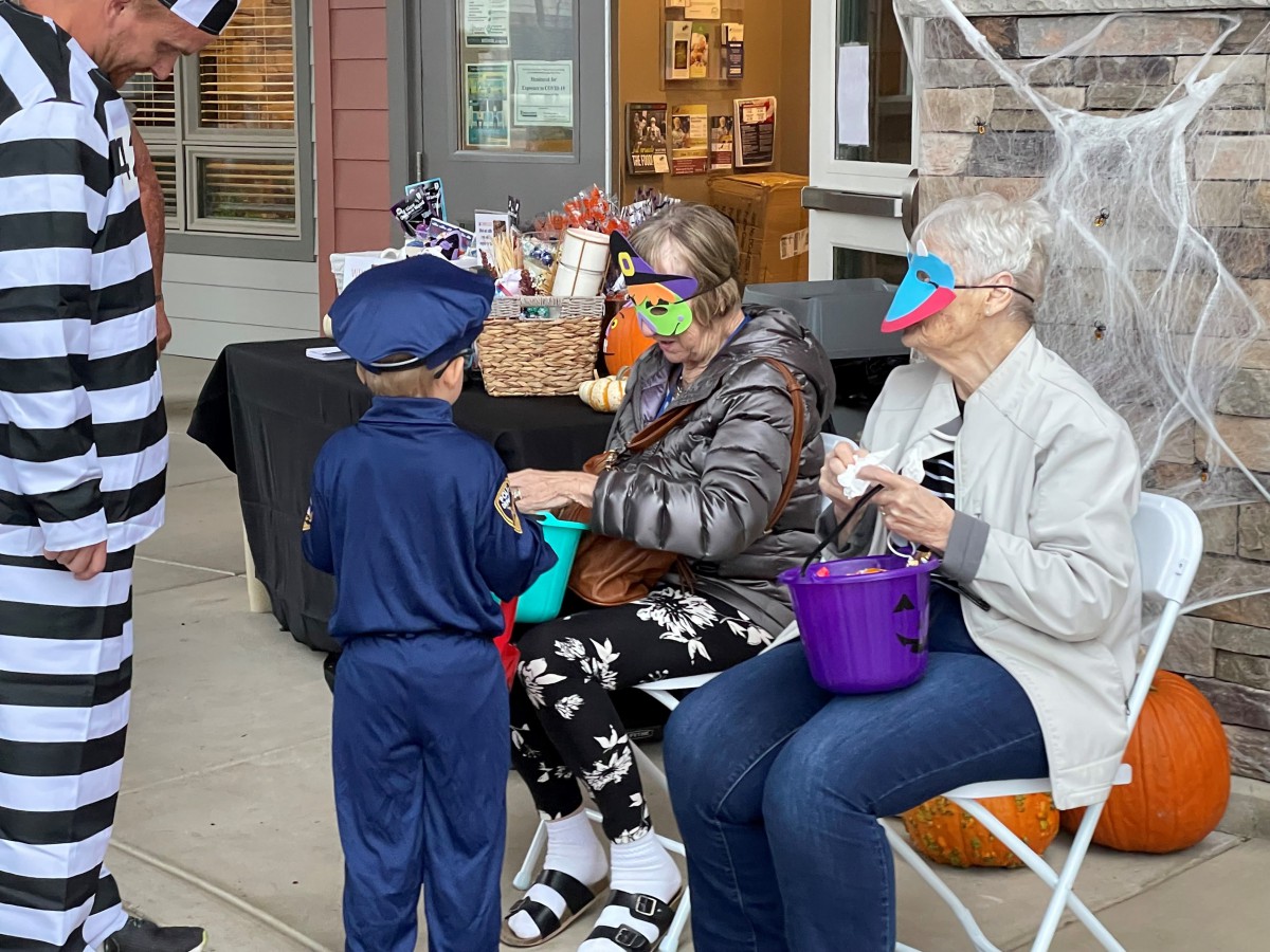 A child in a costume interacts with two seniors wearing masks during a festive Halloween event.