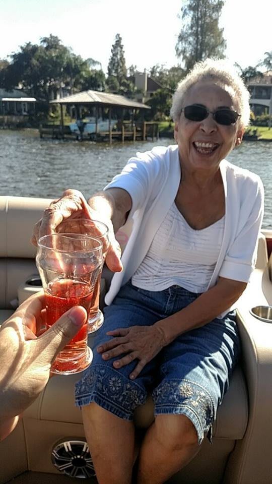 A joyful woman on a boat shares a toast with a friend by the lake.