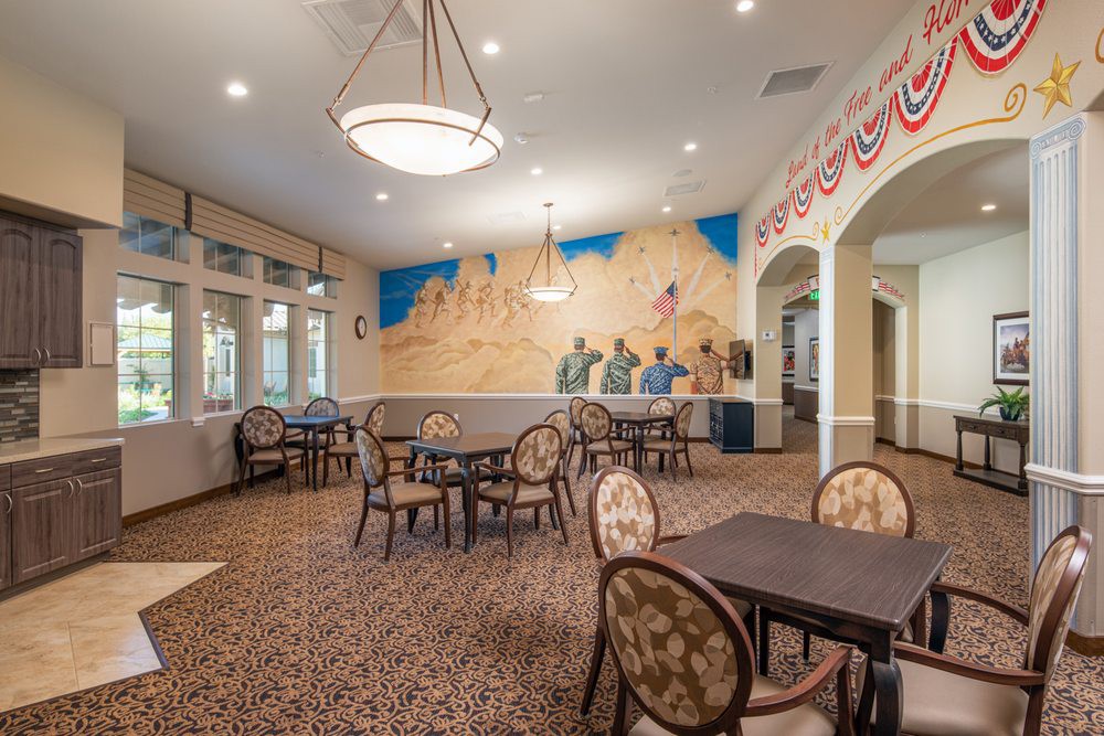 A spacious dining room with multiple tables and chairs, featuring a colorful mural on the wall and elegant lighting fixtures.