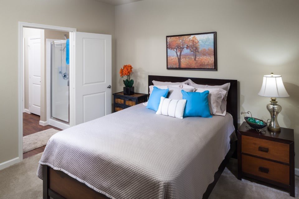 A modern bedroom with stylish decor, featuring a neatly made bed with blue and white pillows and a landscape painting above the headboard.