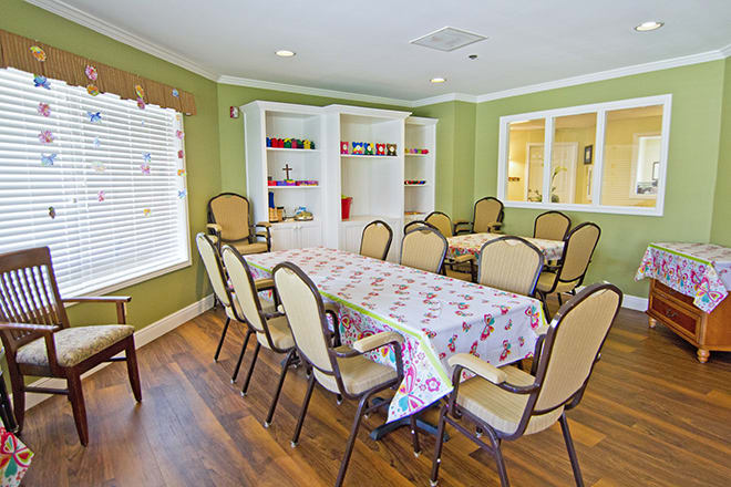 A spacious dining room featuring a long table surrounded by chairs, with green walls and ample natural light.