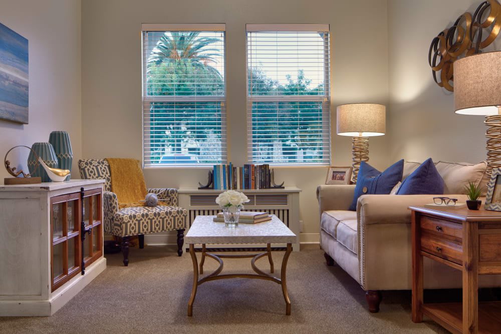 A cozy living room with a sofa, armchair, and coffee table set against a window with blinds.
