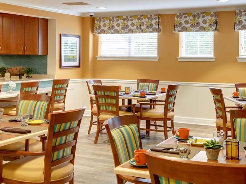 A cozy dining room with neatly arranged tables and chairs, featuring warm decor and natural light from the windows.
