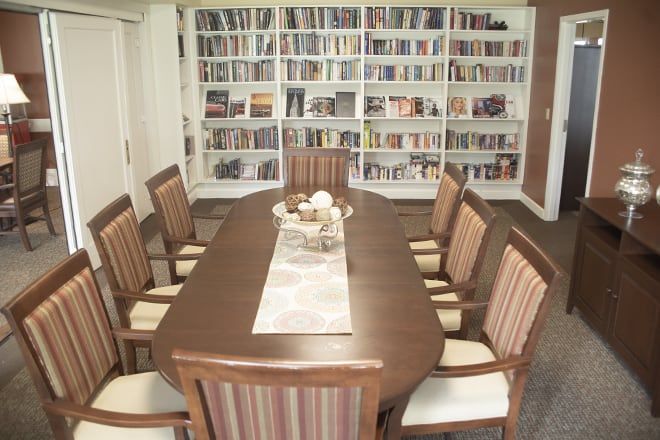 A cozy library room with a long table surrounded by chairs and filled with bookshelves.