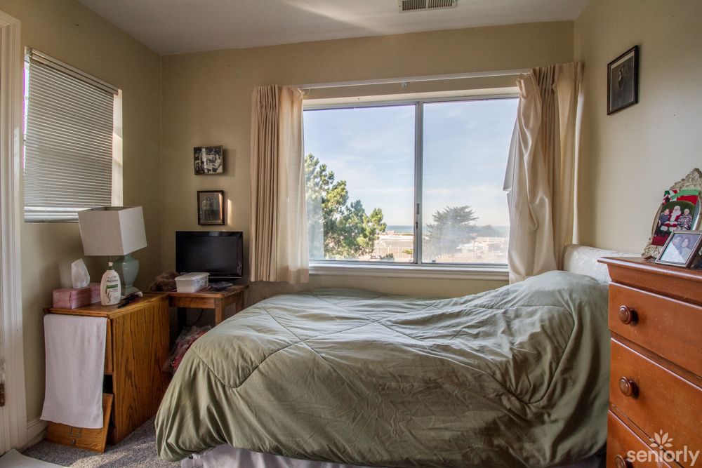 A cozy bedroom with a bed, television, and a large window letting in natural light.