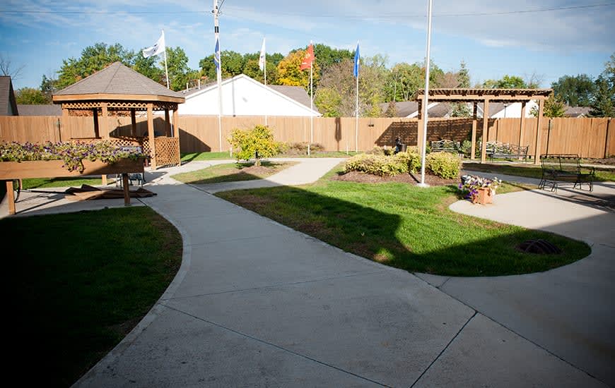 A landscaped garden featuring a winding concrete pathway, greenery, and gazebos on a sunny day.