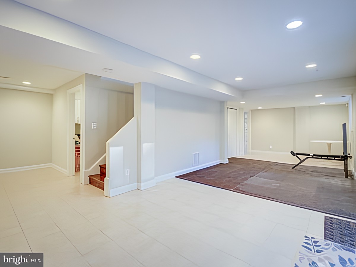 A spacious basement with white walls, featuring a staircase and recessed lighting.