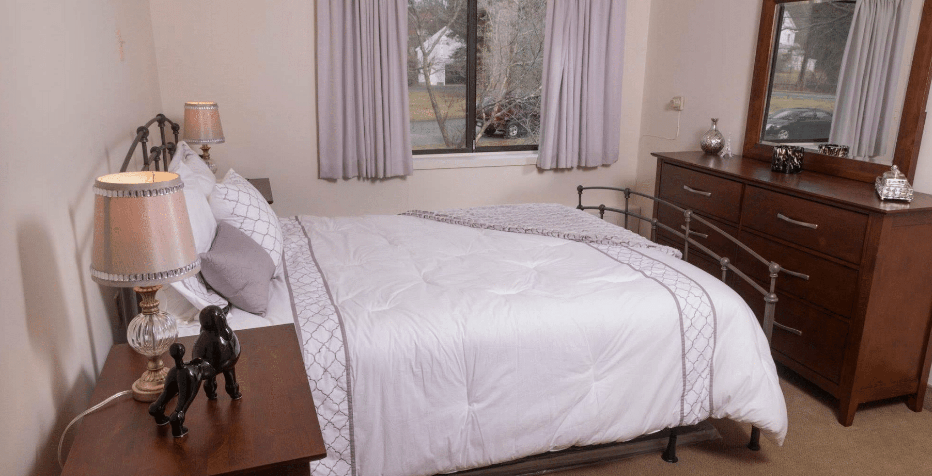 A tidy bedroom with a neatly made bed and curtains drawn near a window.