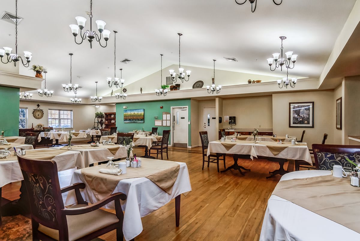 A spacious dining area with neatly arranged tables and chairs, elegant chandeliers, and a warm wooden floor.