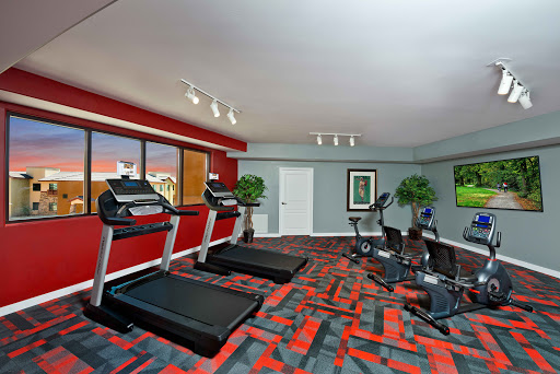 A modern gym area featuring treadmills, elliptical machines, and a vibrant red and grey color scheme.