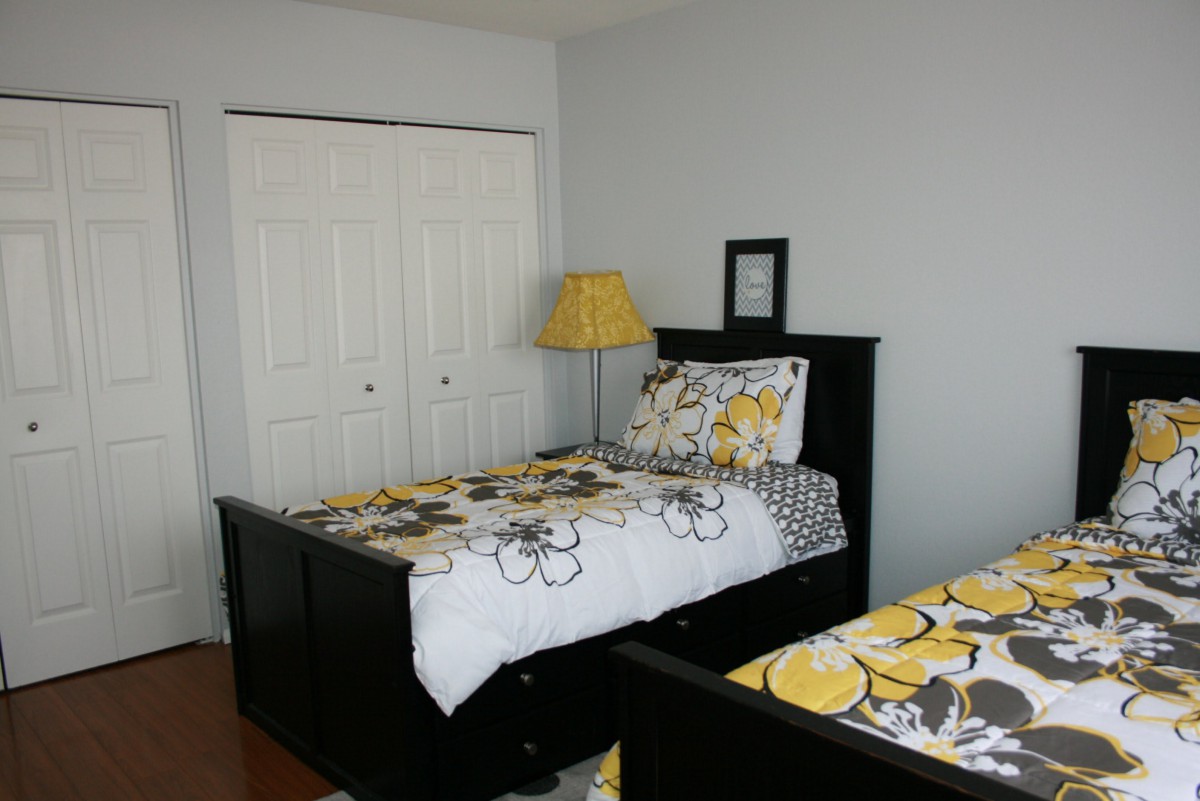 A cozy bedroom with twin beds featuring floral bedding, a lamp, and a closet in the background.