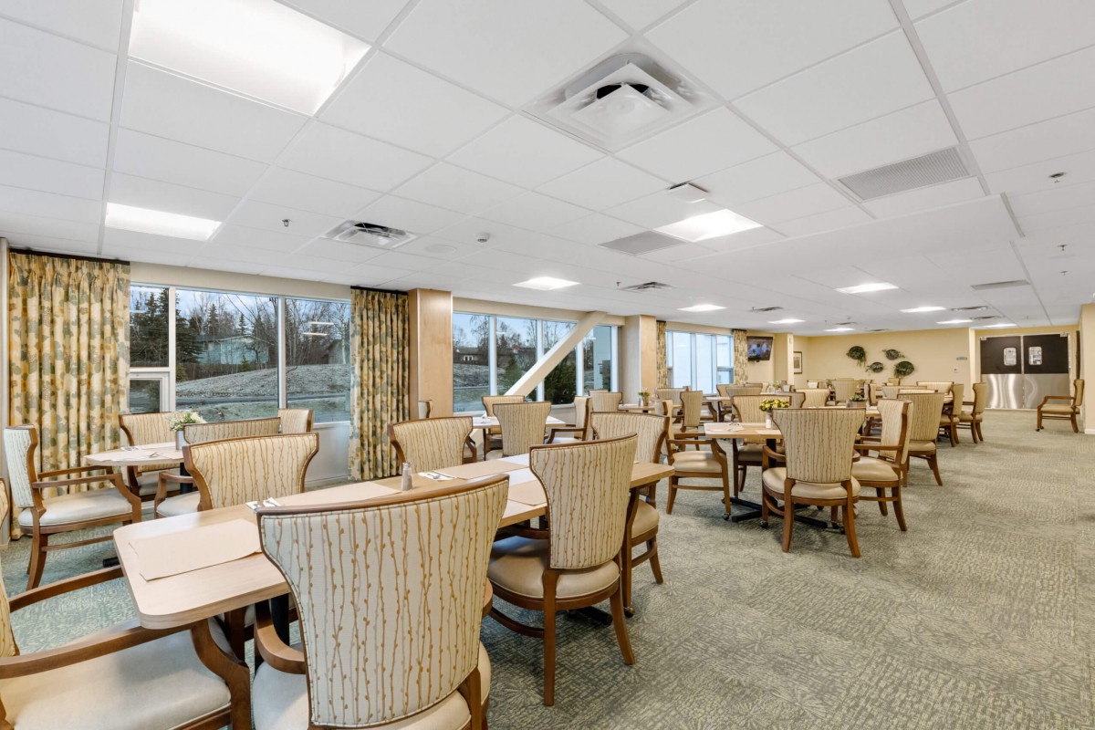 A spacious dining room with several tables and chairs, well-lit by large windows.