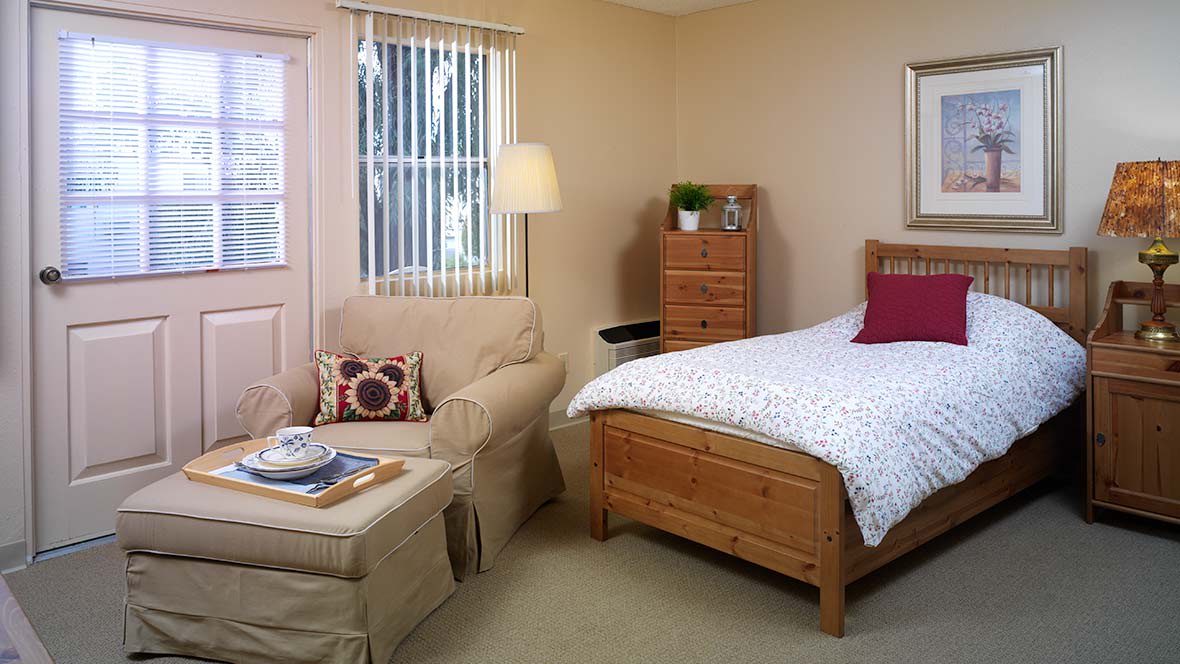 A cozy bedroom with a wooden bed, cushioned chair, and a standing lamp.