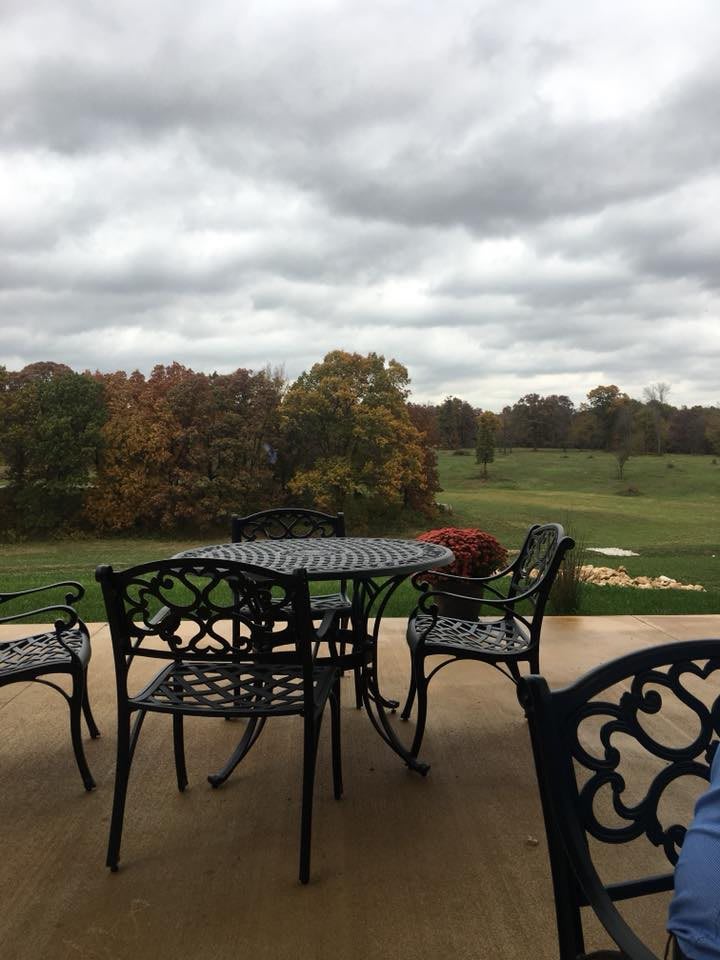 A patio set overlooking a grassy landscape with trees and a cloudy sky.