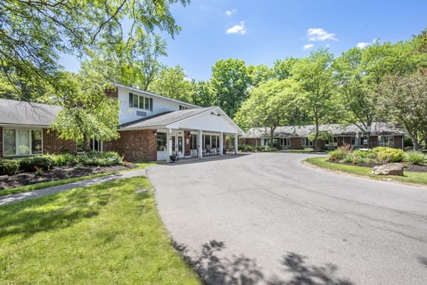 A beautiful residential house with a driveway surrounded by lush trees on a sunny day.