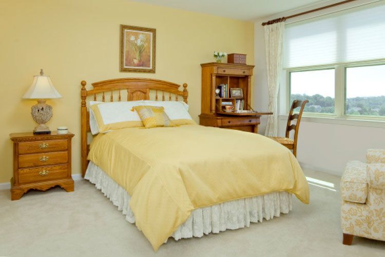 A cozy bedroom with a wooden bed and matching desk, featuring soft yellow tones.