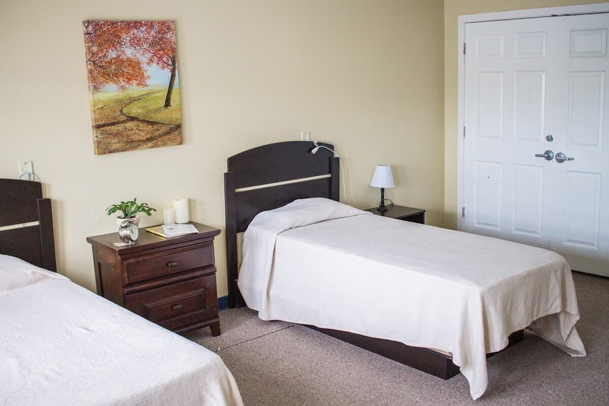 A simple bedroom with twin beds and a bedside table under a painting.