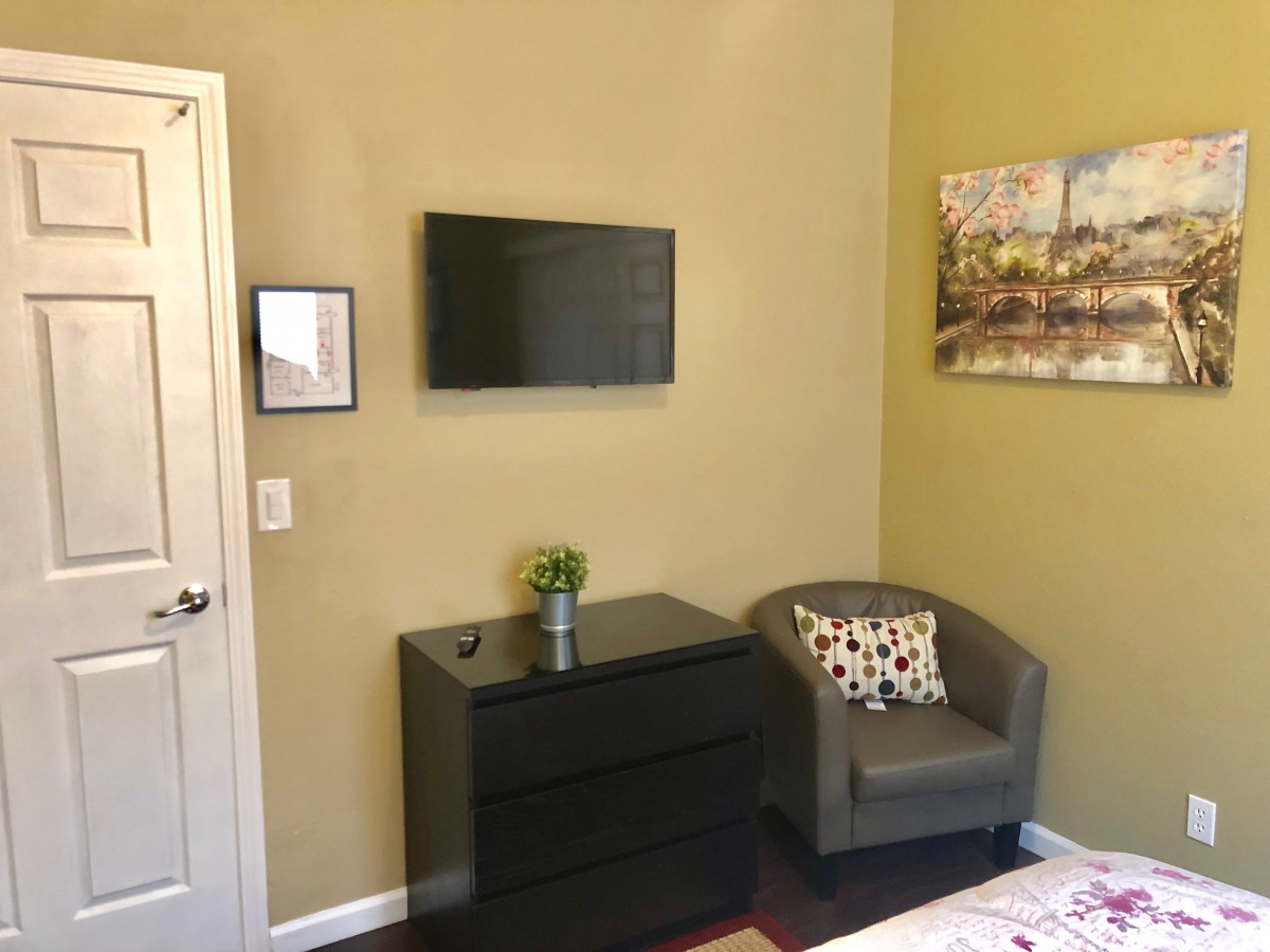 A cozy bedroom corner with a mounted TV, chest of drawers, and armchair.