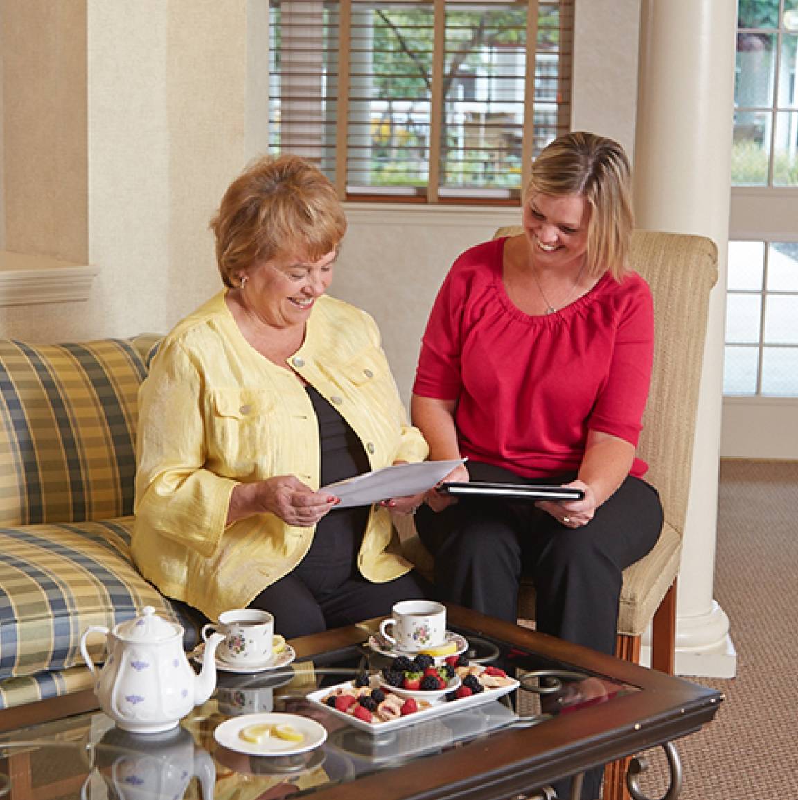 Two women sitting on a sofa, discussing documents over tea.