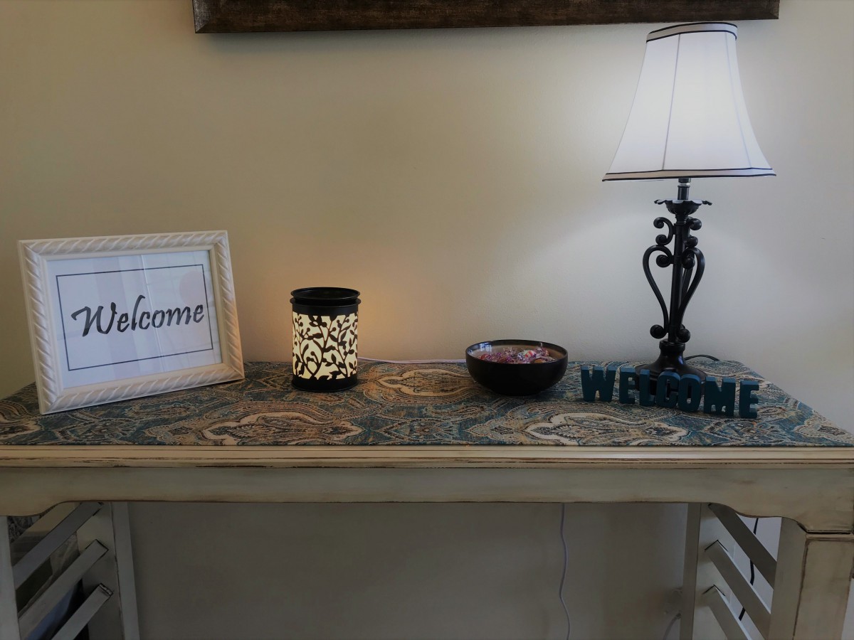 A cozy entryway table with a lamp, welcome sign, and decorative candle.