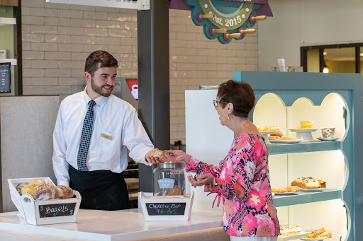 A young man serves an older woman at a cafe, showcasing friendly customer service.