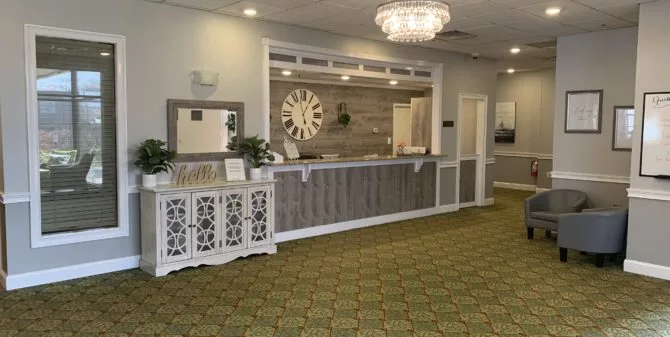 A welcoming hotel lobby with a reception desk and a large wall clock, featuring elegant decor and a chandelier.