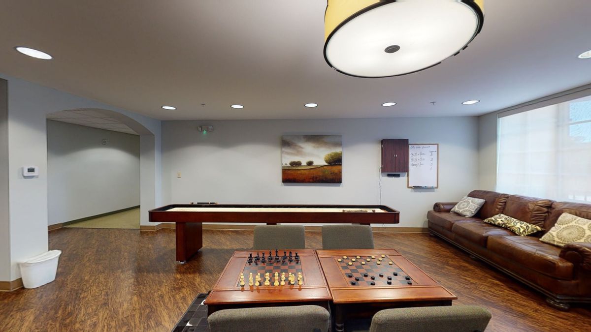 A cozy game room featuring a shuffleboard table, chess and checkers setup, comfortable seating, and stylish decor.