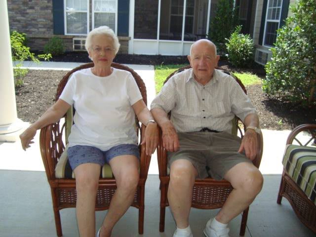 An elderly couple sitting together on outdoor chairs, enjoying the day.