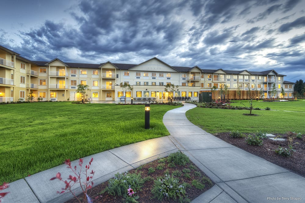 A scenic view of a residential building with a well-maintained lawn and walkway under a dramatic cloudy sky.