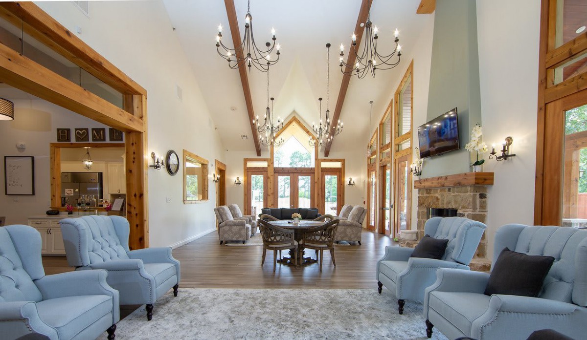 A spacious living room with vaulted ceilings, elegant chandeliers, and abundant natural light through large windows.