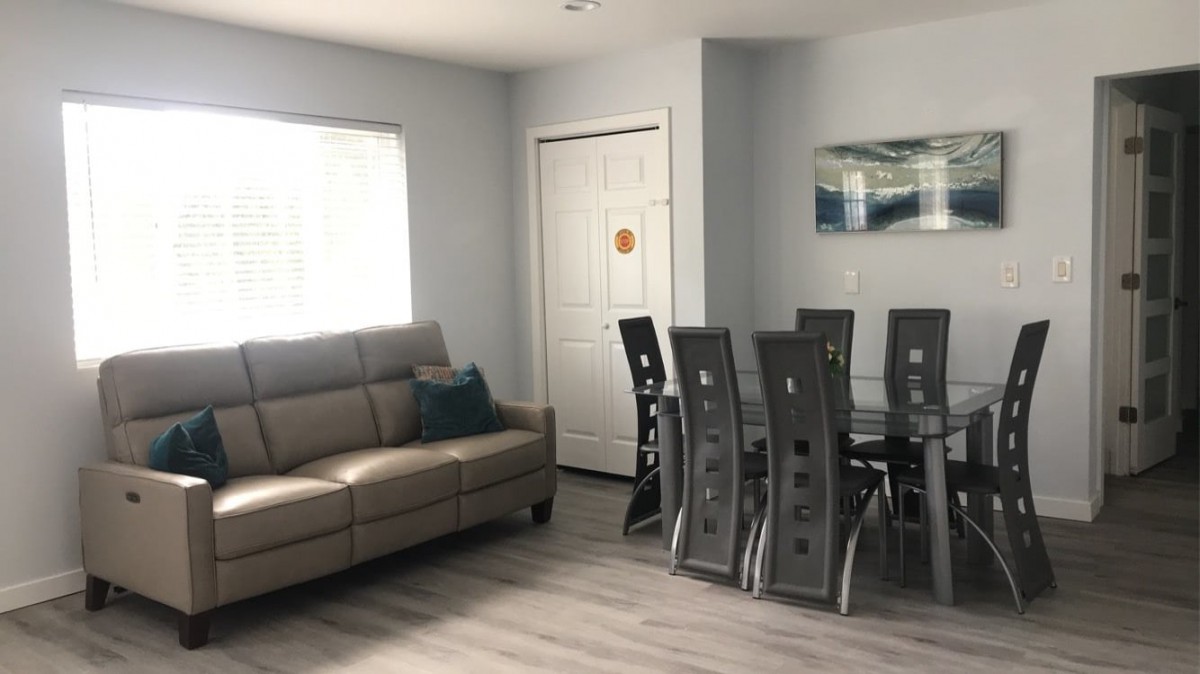 A modern living and dining area featuring a beige sofa and a sleek glass dining table with chairs.