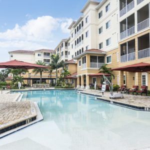 A modern apartment complex with a swimming pool and palm trees.