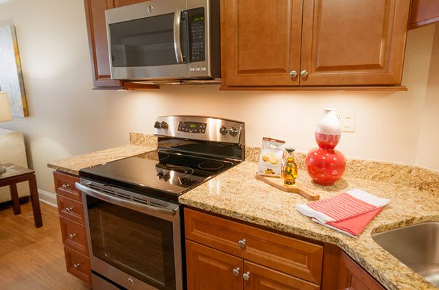 A modern kitchen with wooden cabinets, a stove, and a microwave over a granite countertop.