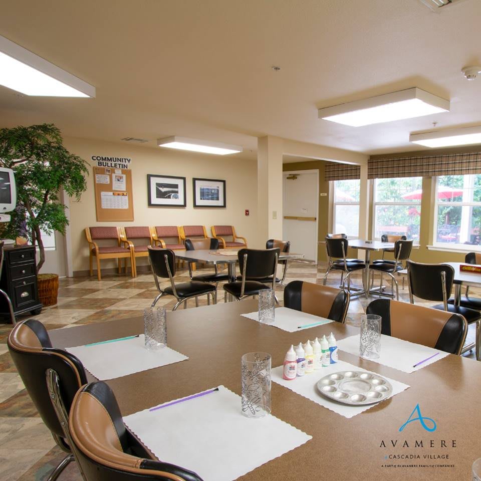 A spacious meeting room with neatly arranged tables and chairs, decorated with plants and artwork on the walls, and illuminated by natural light from large windows.