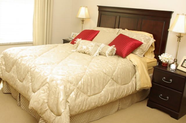 A cozy bedroom with a neatly made bed featuring red accent pillows and a stylish comforter.
