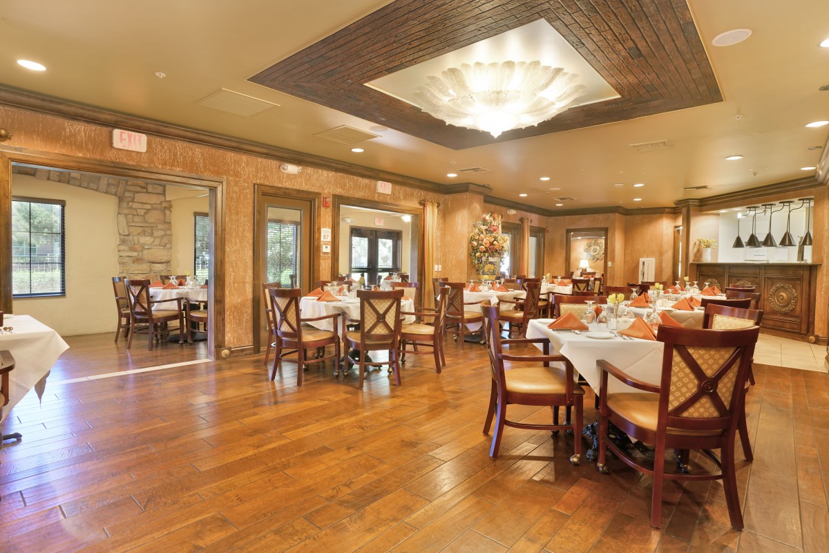 An elegant restaurant dining room with neatly arranged tables and chairs, featuring a warm wooden floor and subtle lighting.