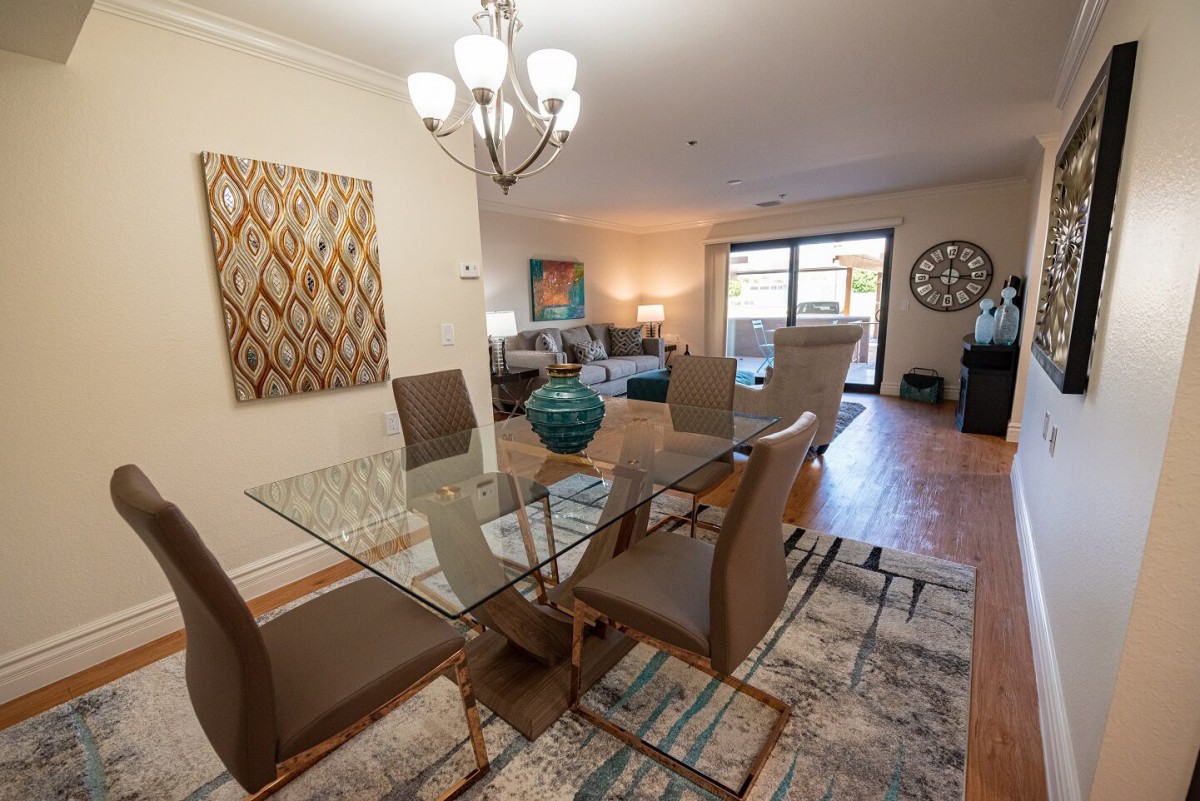 A modern open-plan dining and living room with a glass dining table, contemporary furniture, and decorative artwork.