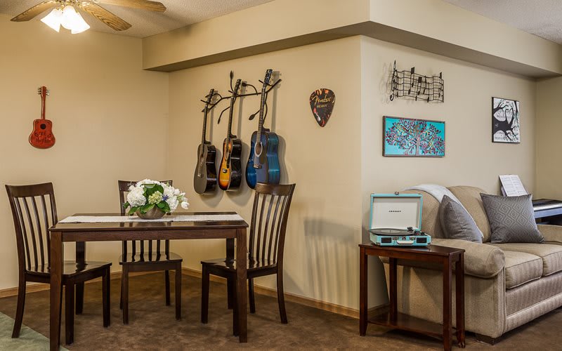 A cozy dining area adorned with hanging guitars, accompanied by a small table and chairs, fresh flowers, and a turntable for music enthusiasts.