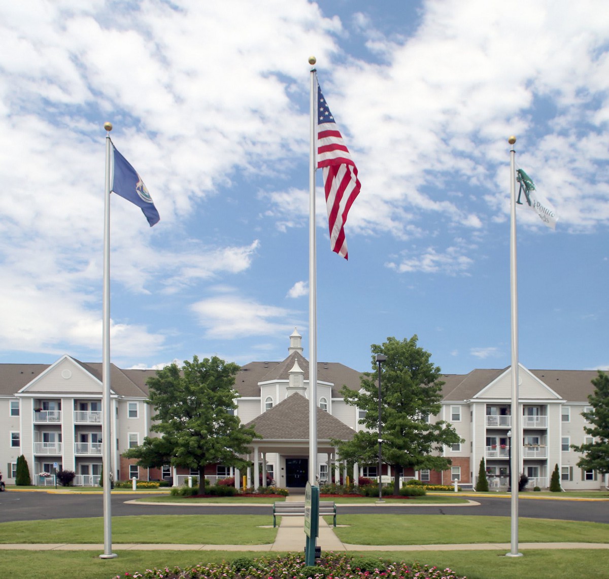 A building with three flagpoles and a landscaped foreground under a cloudy sky.